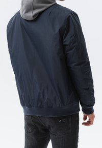 Marinblå bomberjacka med grå huva, dragkedjestängning, elastiska ärmslut och nederkant. Slät, lätt glänsande tyg med minimala sömnadsdetaljer.