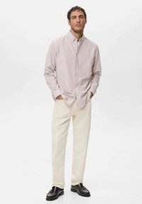 Camisa rosa claro abotonada con cuello clásico, combinada con pantalones color crema y mocasines oscuros. Diseño simple y limpio.