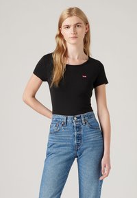 Black short-sleeve fitted t-shirt with a small red Levi's logo, paired with high-waisted light blue denim jeans. Smooth texture, crew neck design.
