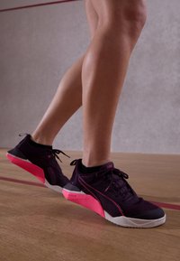 Zwarte en roze sportieve schoenen met een gestructureerde bovenkant, ronde neus en een gedurfde, hoekige roze hak. Veters en branding in contrasterende kleuren.