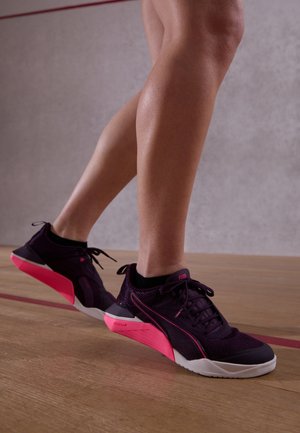 Chaussures de sport noires et roses avec une tige texturée, un bout arrondi et un talon rose audacieux et angulaire. Lacets et marquage dans des couleurs contrastées.