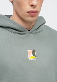 Πράσινο φούτερ με κουκούλα και τσέπη καγκουρό, με πολύχρωμο λογότυπο στο στήθος. Κατασκευασμένο από μαλακό ύφασμα με ομαλή  υφή.