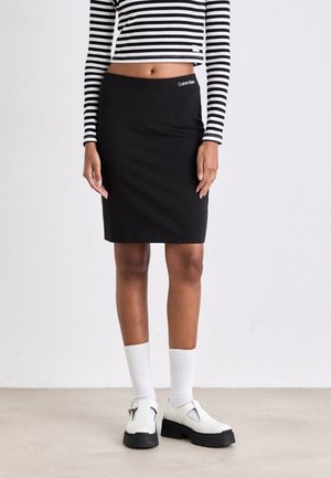 Woman wearing a black knee-length Calvin Klein skirt, black-and-white striped long-sleeve crop top, white socks, and white platform shoes.