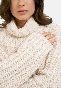 Cremfarbener Strickpullover mit hohem, geripptem Rollkragen. Verfügt über eine strukturierte Naht und offene Bündchen, die ein weiches, voluminöses Garn zur Schau stellen.