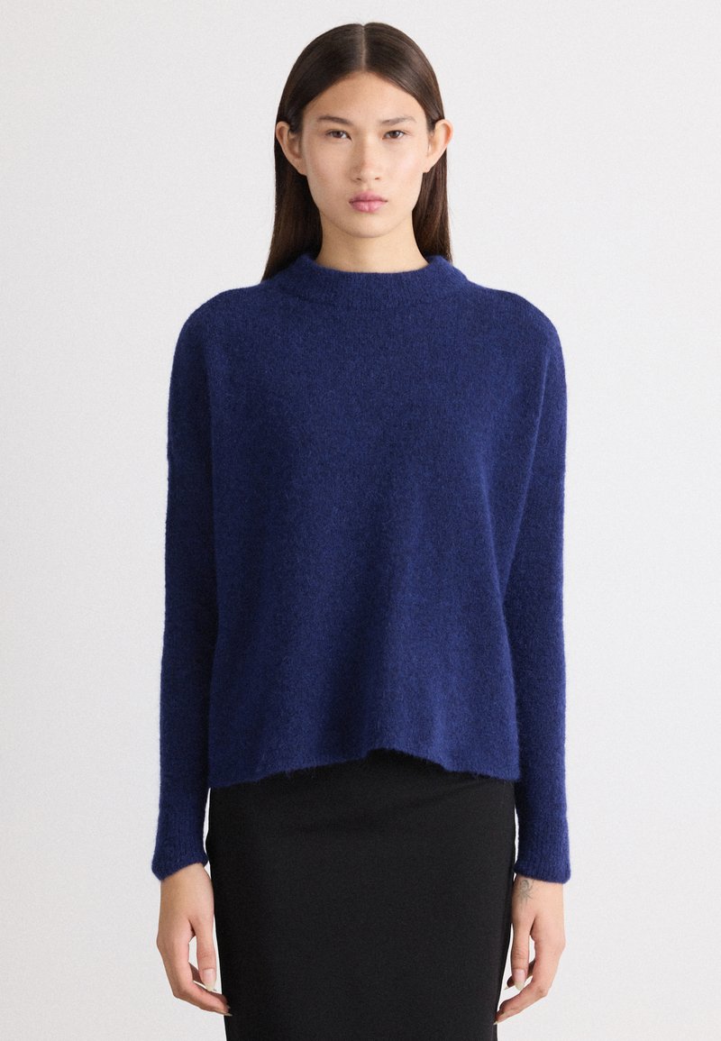 Maglione peloso blu navy con un alto collo, maniche lunghe e vestibilità rilassata; presenta un orlo corto e una texture morbida.