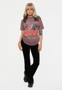 AC/DC graphic t-shirt in maroon featuring a colorful spider design, paired with black velvet flared pants and black boots.