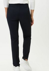 Pantaloni neri aderenti realizzati in tessuto liscio, con vita alta media, due tasche posteriori e gamba affusolata, abbinati a sneakers bianche.