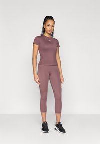 Pielāgots sporta tops un īsie legingi mauve krāsā, izgatavoti no elastīgas auduma. Iekļauj mazu logo uz krūškurvja un sānos legingiem.