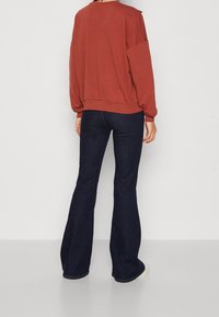Svetřík barvy rezavé s povolenými rameny, žebrovaným lemem a širokými rukávy, kombinovaný s tmavými rozšířenými džínami. Výrazné švy na džínách.