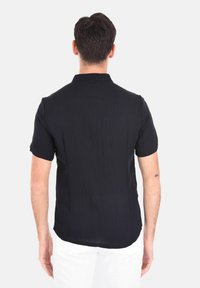 Camicia blu navy a maniche corte realizzata in tessuto leggero, con colletto a punta e orlo dritto, caratterizzata da una texture liscia e linee pulite.