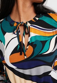 Wielokolorowa bluzka z kwiatowym wzorem, z dekoltem typu łezka, z wiązaniami przy kołnierzyku i gładkiego, lekkiego materiału.