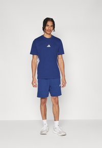 L'ensemble de vêtements de sport bleu marine comprend un T-shirt à manches courtes et un short, avec des accents blancs à trois rayures et un logo sur la poitrine et la cuisse.