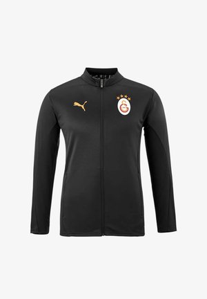 Schwarze Sportjacke aus glattem Stoff, mit hohem Kragen, durchgehendem Reißverschluss, Puma-Logo in Gold und einem Mannschaftswappen mit Sternen auf der Brust.