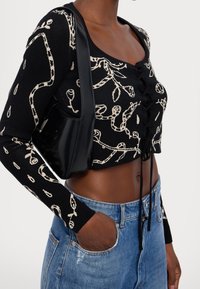 Femme portant un haut court noir à motifs floraux blancs, un jean bleu clair et un sac à bandoulière noir.