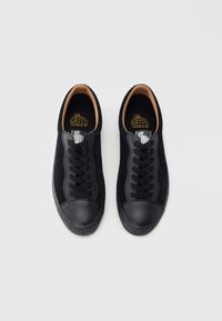 Czarne trampki z zamszową cholewką, gumowym noskiem i fakturowaną podeszwą. Posiadają czarne sznurówki i logo na wkładce. Prosty, niskoprofilowy fason.