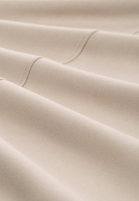 Lichtbeige stof met een gladde textuur, voorzien van subtiele ribbels en netjes gestikte randen, in zachte plooien gerangschikt.