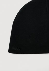 Czarna dzianinowa czapka beanie z subtelnym haftem logo "HUGO" przy krawędzi, prezentowana na jednolitym jasnym tle.