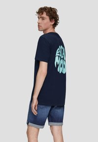 Navyblauwe katoenen t-shirt met een grote lichtblauwe "ESCAPE MOOD" grafiek op de achterkant, gecombineerd met denim shorts.