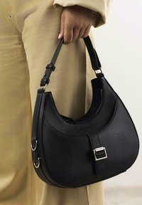 Bolso de mano de cuero negro con una silueta redondeada, que cuenta con una textura suave, herrajes de hebilla plateada y una correa desmontable.
