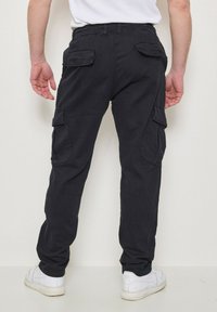 Pantalons cargo noirs avec taille ajustable, plusieurs poches, coupe droite et en coton. Portés avec des baskets blanches.