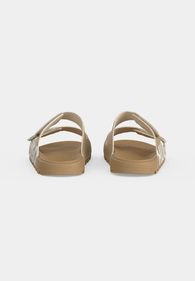 Paire de sandales slides beige à bouts ouverts avec deux sangles réglables et texte blanc sur les côtés, vues de dos sur fond blanc.