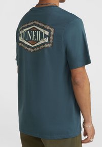 Vīriešu zils kokvilnas T-krekls ar ģeometrisku O'Neill logo baltā un brūnā krāsā aizmugurē; īsas piedurknes un apaļa kakla izgriezuma forma.