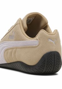 Μπεζ παπούτσι από σουέτ με υφή, που διαθέτει λευκή ρίγα και λογότυπο Puma, στρογγυλεμένη πίσω όψη και μαύρη ελαστική σόλα με ανάγλυφο μοτίβο.