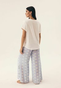 Biała koszulka z rozwiniętymi rękawami zestawiona z jasnoniebieskimi spodniami o szerokim kroju z chmurowymi wzorami. Strój jest casualowy i luźny w stylu.