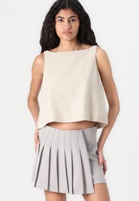 Bežový cropped top z mäkkej, textúrovanej tkaniny; v kombinácii s svetlošedou plisovanou mini sukňou s viacerými ostrými záhybmi a hladkým pásom.