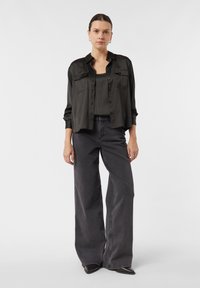 Schwarzes Satinhemd, schwarzes Tanktop und dunkelgraue Jeans mit weitem Bein. Flache schwarze Schuhe, minimalistisches Design, ohne sichtbare Muster oder Akzente.