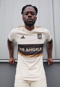 Maglietta da calcio bianca con strisce orizzontali marroni e dorate, testo "LOS ANGELES", logo Adidas e emblema della squadra. Texture liscia, vestibilità atletica.