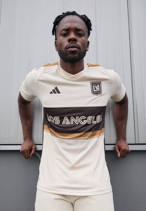 Maillot de football blanc avec des rayures horizontales marron et dorées, texte "LOS ANGELES", logo Adidas et emblème de l'équipe. Texture lisse, coupe athlétique.