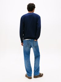 Felpa navy con tessuto testurizzato, vestibilità morbida, abbinata a jeans azzurri chiari con design classico a cinque tasche, indossata con sneakers marroni.
