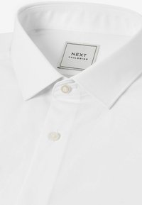 Camisa blanca de botones confeccionada en una tela suave, con un collar clásico, dos botones en el cuello y una etiqueta minimalista en el interior.