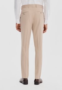 Beżowe spodnie materiałowe o dopasowanym kroju, podwójne tylne kieszenie z zapięciem na guziki, gładki materiał i prosta nogawka.
