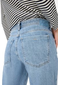 Light blue denim jeans with two back pockets, slightly curved seams, and subtle stitching details. Paired with a black and white striped shirt.