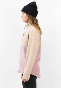 Fleece sweatshirt in beige en roze met een rits tot een kwart, zijzakken en lange mouwen. Gekozen met een zwarte gebreide beanie.
