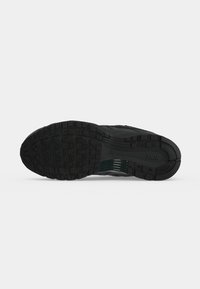 Semelle de chaussure Nike noire avec motif de bande de roulement texturé et logo visible, vue de dessous sur un fond blanc uni.