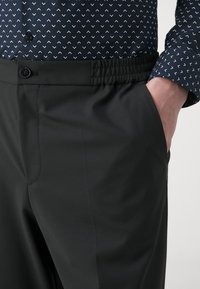 Sorte bukser laget av et glatt, lett stoff med flat front, elastisk midje og sidelommer for komfort og praktisk bruk.