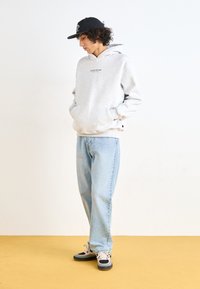 Hoodie gris clair avec le texte "STUDIO EDITION", associé à un jean bleu clair et des baskets noires et roses. Texture de tissu lisse, coupe décontractée.