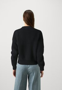 Schwarzer gestrickter Pullover mit strukturierter Oberfläche, Rundhalsausschnitt und leicht oversized Passform, kombiniert mit hellblauen weit geschnittenen Jeans.