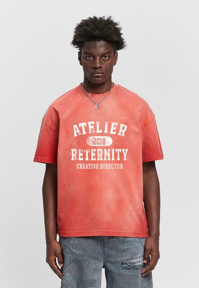 T-shirt en coton rouge avec un col rond, arborant le texte blanc "ATELIER RETERNITY 2018 DIRECTEUR CRÉATIF" dans une police vieillie. Coupe décontractée.