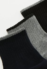 Trzy pary skarpetek: jedna całkowicie czarna, jedna ciemnogranatowa i jedna szara o prążkowanej fakturze. Każda z nich ma kontrastowe prążkowane ściągacze.