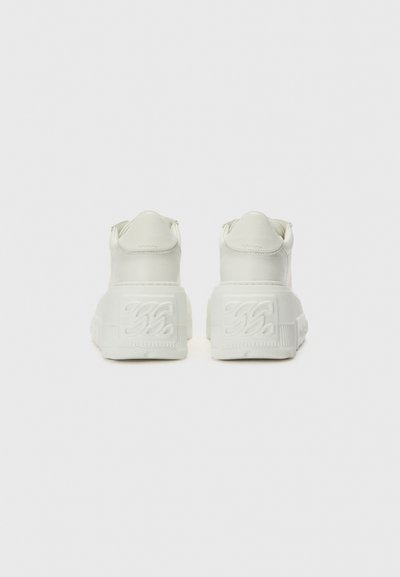 White platform sneakers with a textured sole and embossed logo detail on the heel. Smooth synthetic upper and rounded rear design.