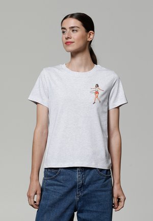 T-shirt en coton gris avec une figure féminine imprimée portant un cerceau sur le côté gauche de la poitrine. Col rond et manches courtes.
