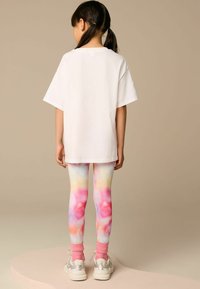T-shirt bianco oversize abbinato a leggings tie-dye multicolori con sfumature di rosa, giallo e blu. Calzini alla caviglia rosa e sneakers argento.
