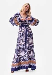 Sukienka maxi w kremowo-granatowy wzór zebry, z długimi puff sleeves, wiązaniem w talii oraz falbaną na dole z brązowym akcentem. Miękka tkanina.