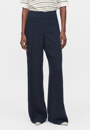 Femme portant un pantalon taille haute à jambes larges bleu marine associé à un haut à manches courtes rayé blanc et noir.