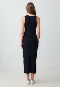 Robe midi côtelée bleu marine avec une silhouette ajustée, sans manches et une texture subtile. Associée à des baskets blanches.