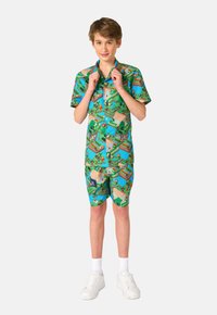 Camisa de manga corta con botones y pantalones cortos a juego en un verde vibrante con un patrón de paisaje pixelado; material de algodón; zapatillas blancas.